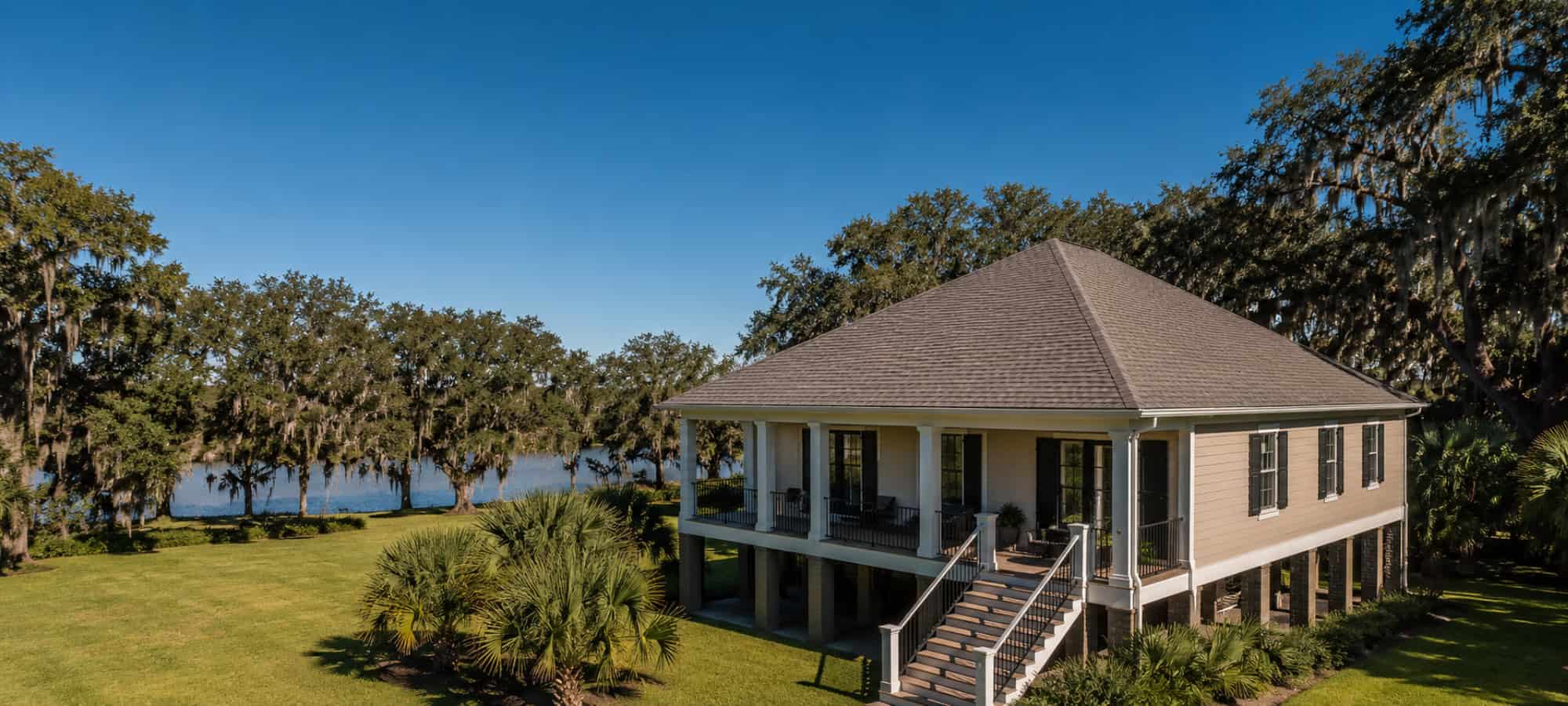 An elevated Louisiana home with a hip roof and full-width porch on a lawn beside the water.